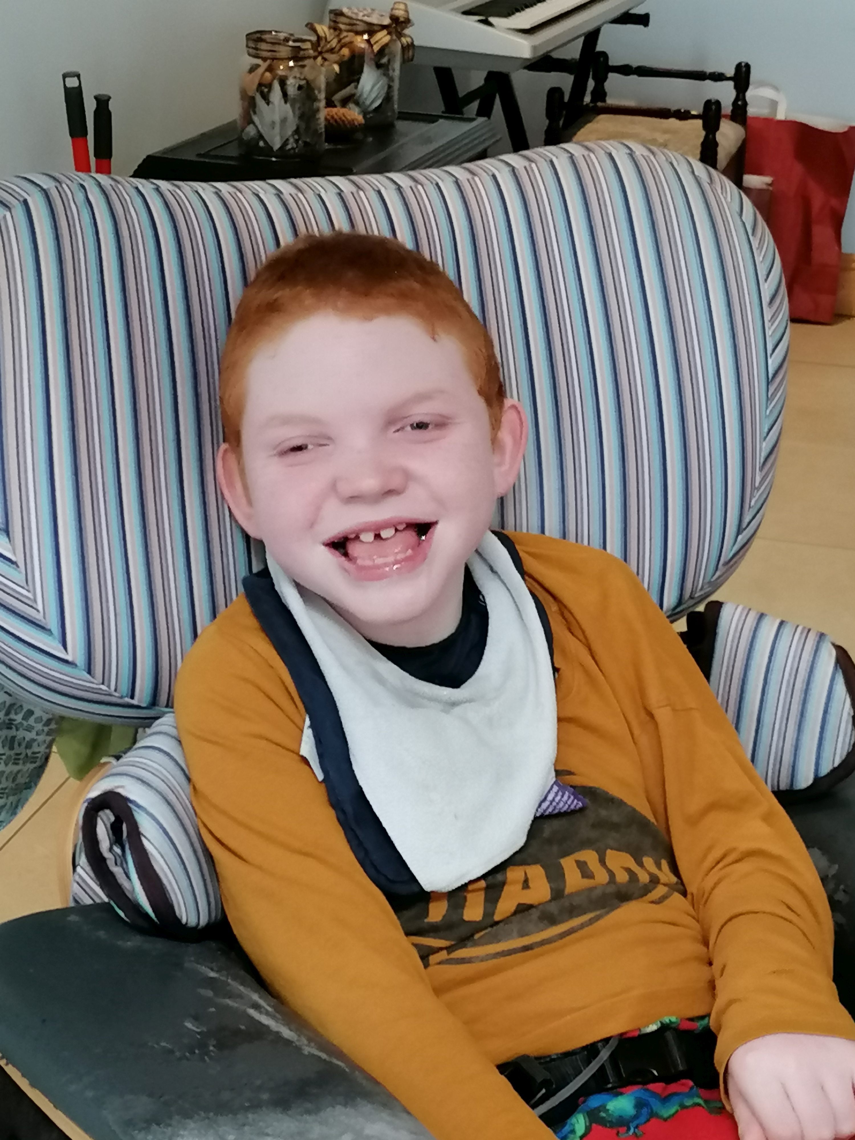 The image shows a smiling Harry Cullen at home, sitting in his chair, wearing an orange top
