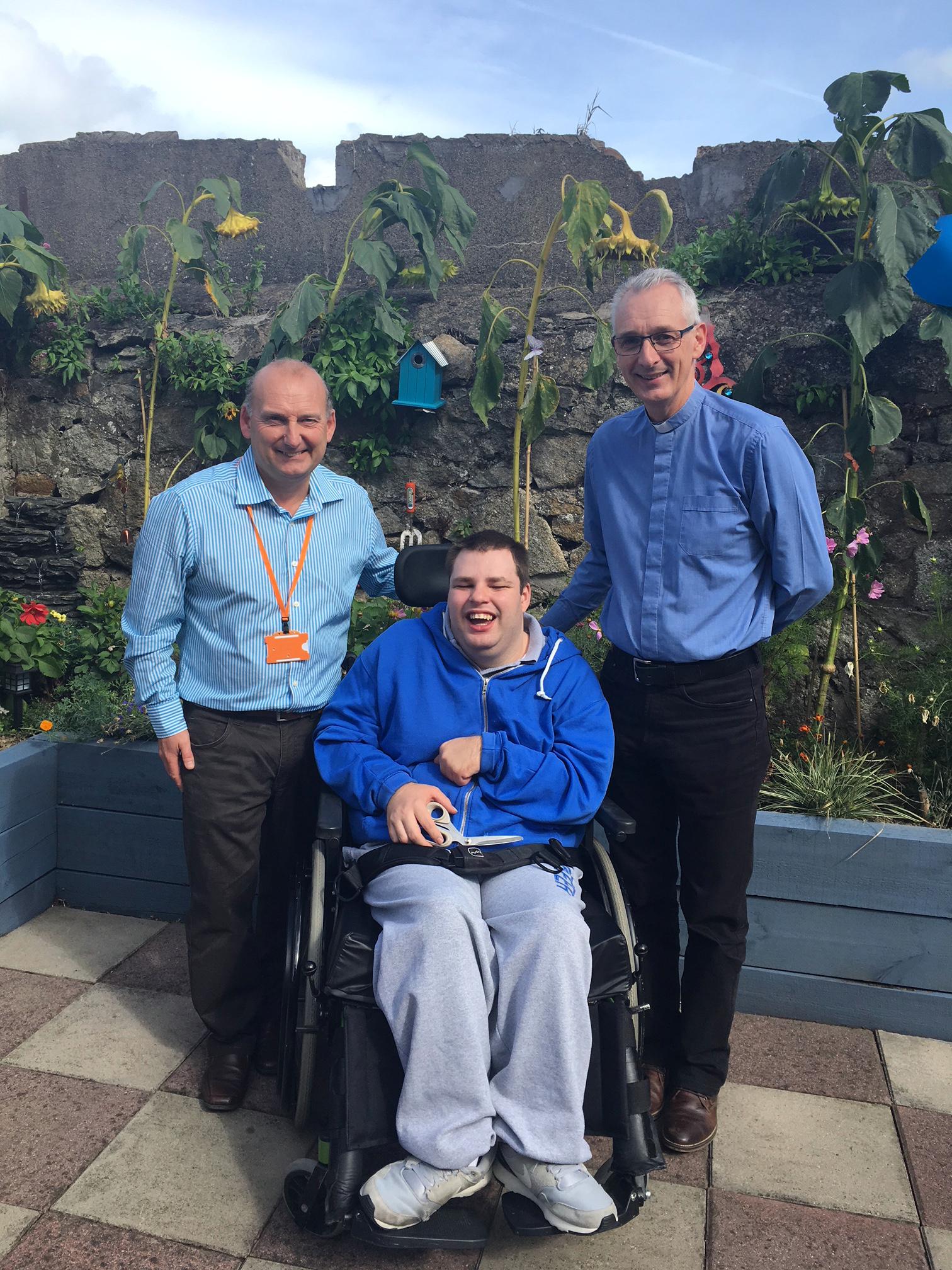 Gary Morris, Alan Koppenhofer and Rev. David Nixon at the official opening of the Sensory Garden in Enable Ireland Dun Laoghaire Adult Services on 13th September Two men and one wheelchair user in front of a sunny garden wall